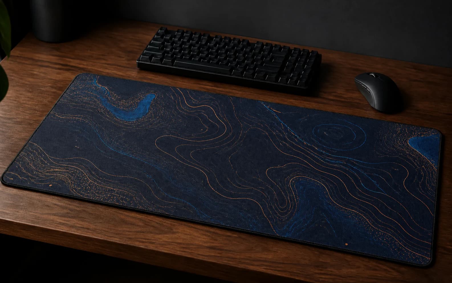 Custom gaming desk mat with navy and copper topographic artwork on a walnut desk