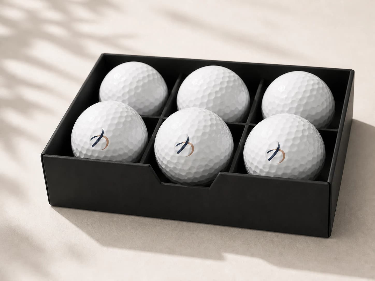 Six custom golf balls with small navy and copper printed marks in a black presentation tray
